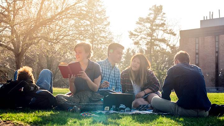 Students on the commons lawn, sun setting, smiling and chatting together, reading books.