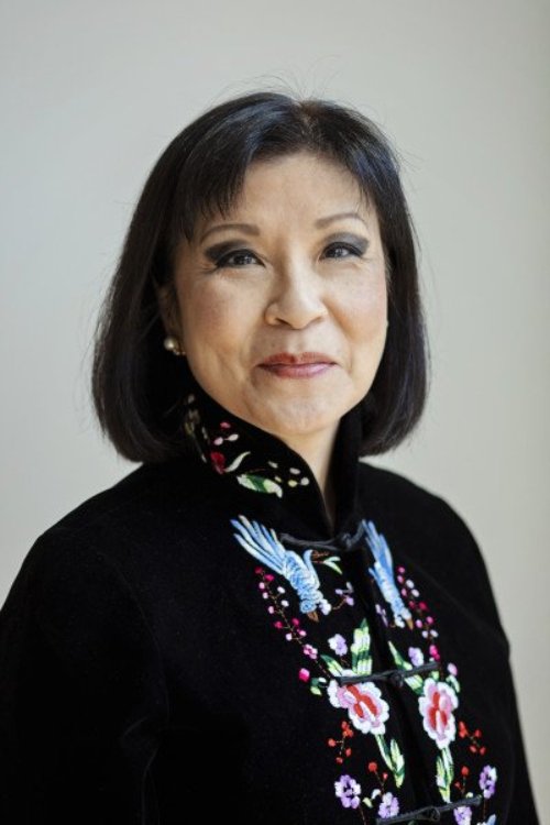 Pearl, an Asian woman with short black hair, wears a black suit jacket with an ornate pattern in a professional headshot with grey background.