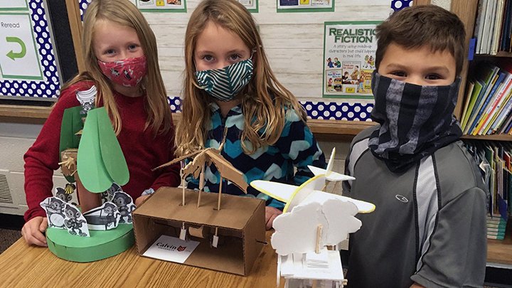 Three second-grade students pose with automatas made by Calvin University engineering students.